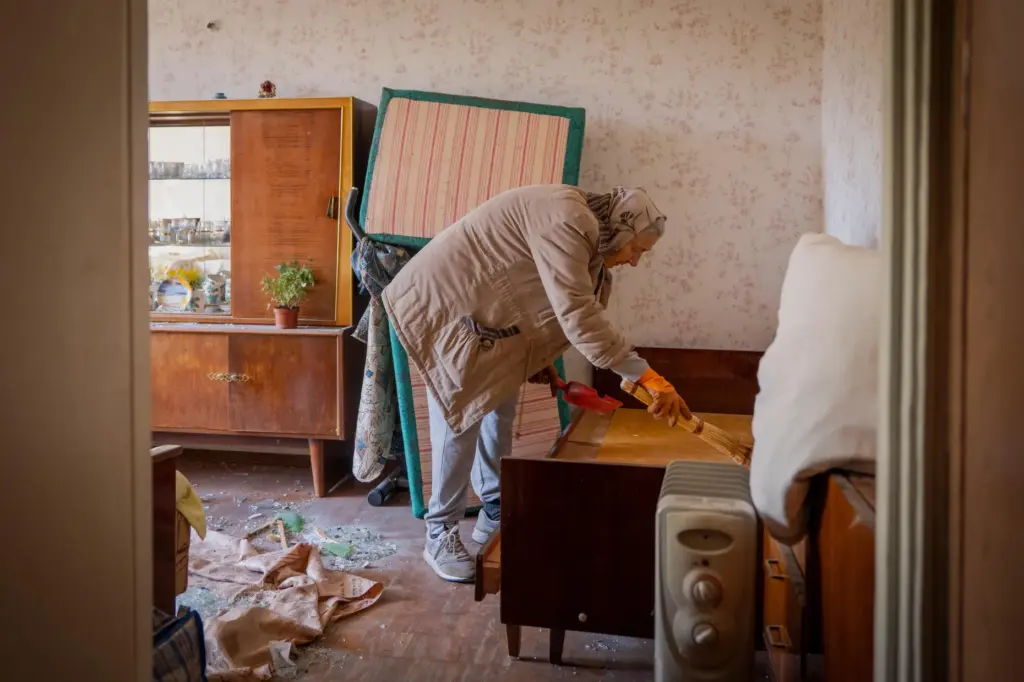 A woman cleans her apartment after a Russian missile exploded near her home in Kyiv.