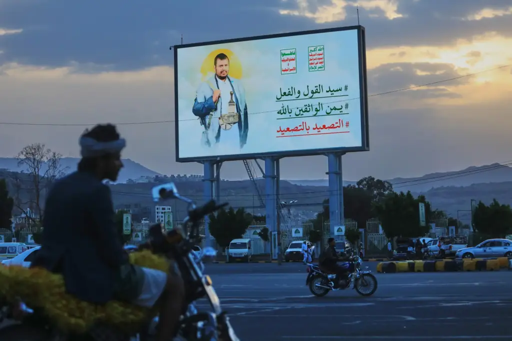 People ride their motorbikes under a billboard showing Houthi leader Abdul Malik al-Houthi.
