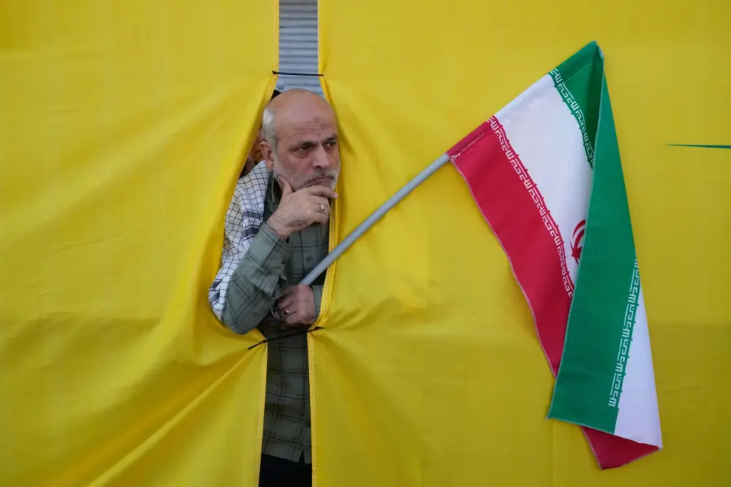A man holding an Iranian flag peers through an opening in a curtain.