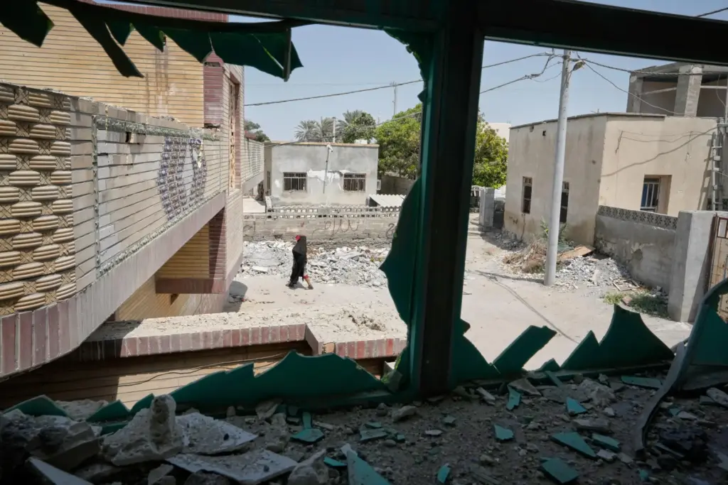A person walks past debris, seen through a shattered window...