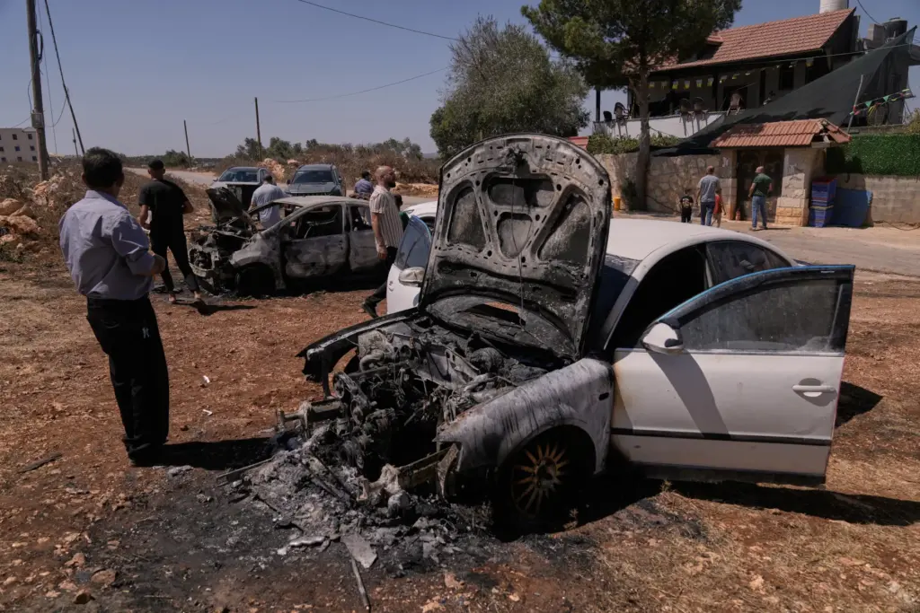 Palestinians stand next to burned cars following an attack by Israeli settlers.