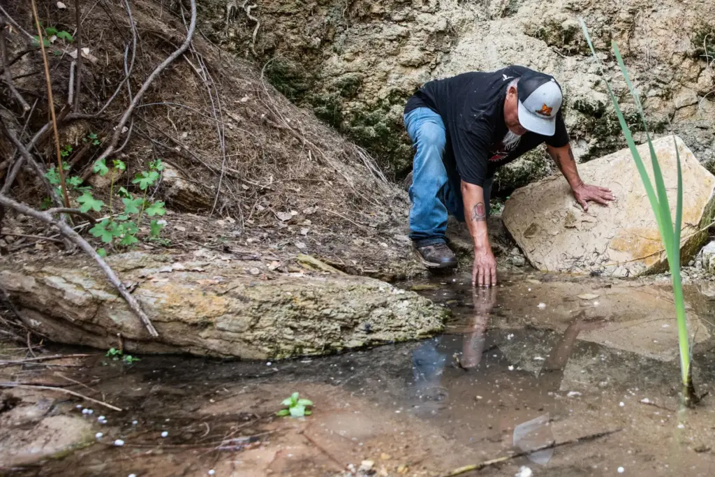Malcolm Lehi touches the cool water of Entrance Spring.