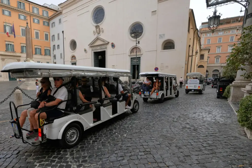 A flotilla of golf carts carrying tourists travels past the Basilica of Santa Maria sopra Minerva.