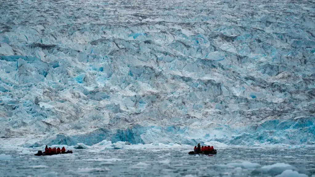 Two groups from the Poseidon Expeditions tour company look at a glacier.