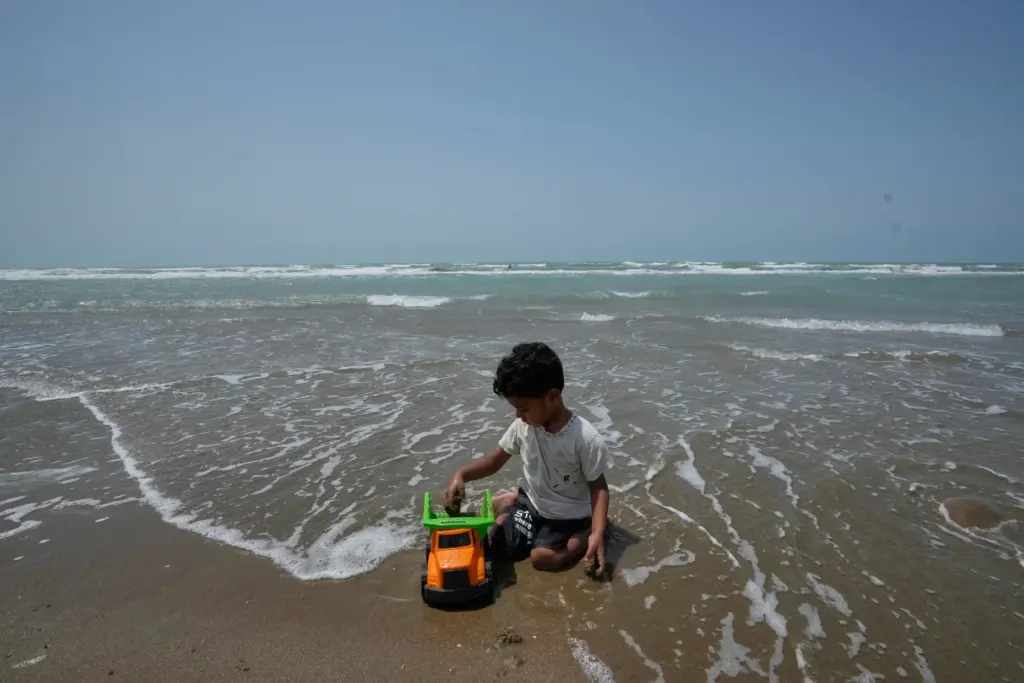 A boy plays with a toy truck on a beach...