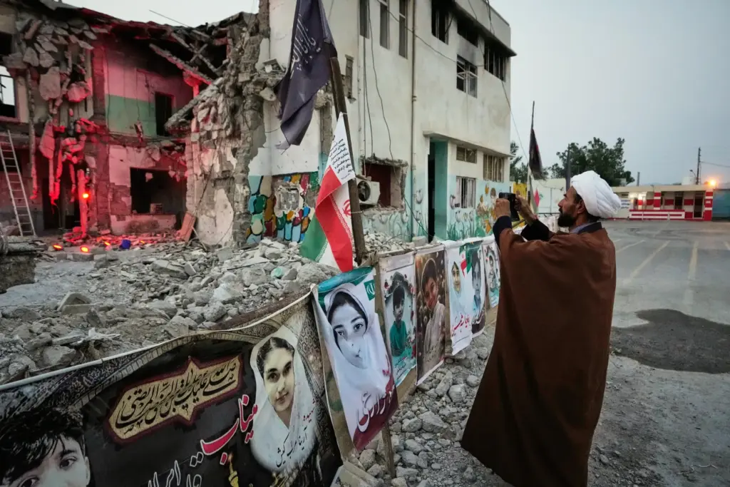 A cleric takes a photograph at the shattered Shajareh Tayyebeh...