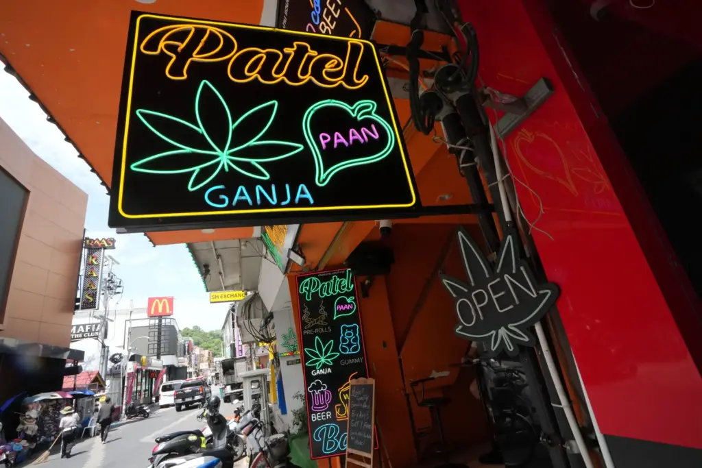 Workers clean a road next to a sign of a cannabis shop in Pattaya, Thailand.
