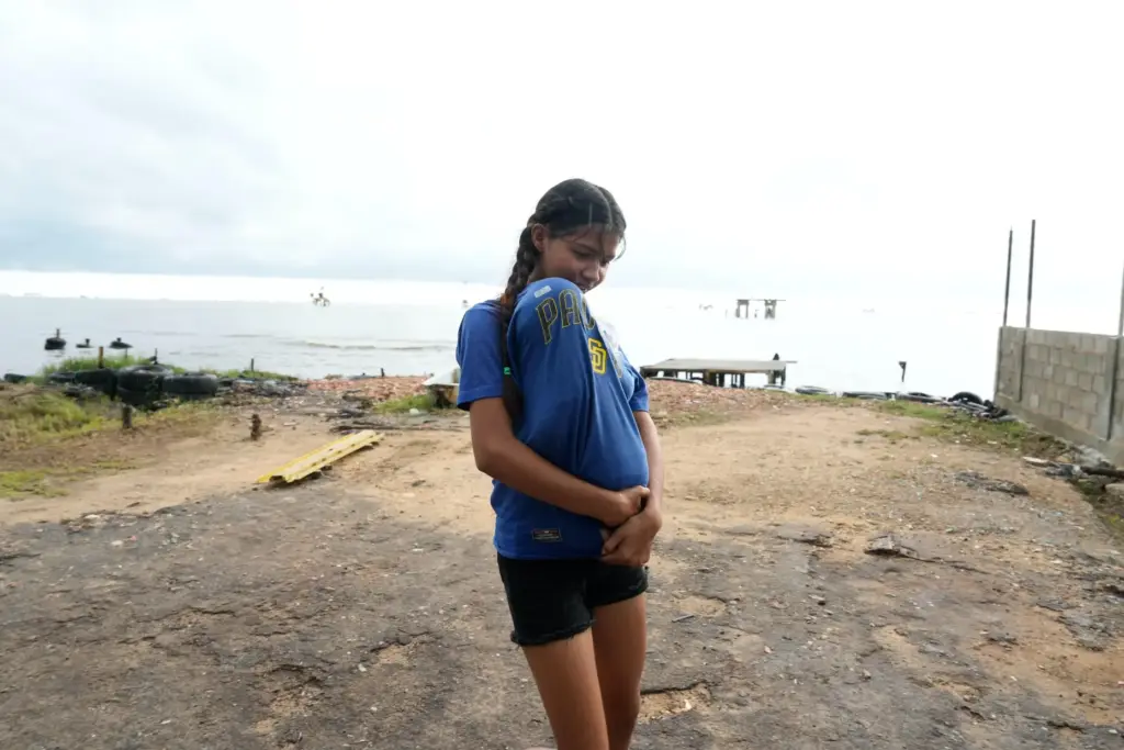 A woman covering a child from the rain walks along the shore of Lake Maracaibo.