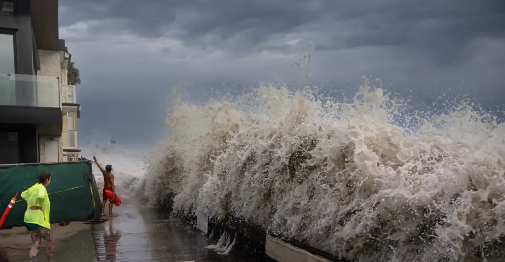 Waves pound a small retaining wall during high tide as...
