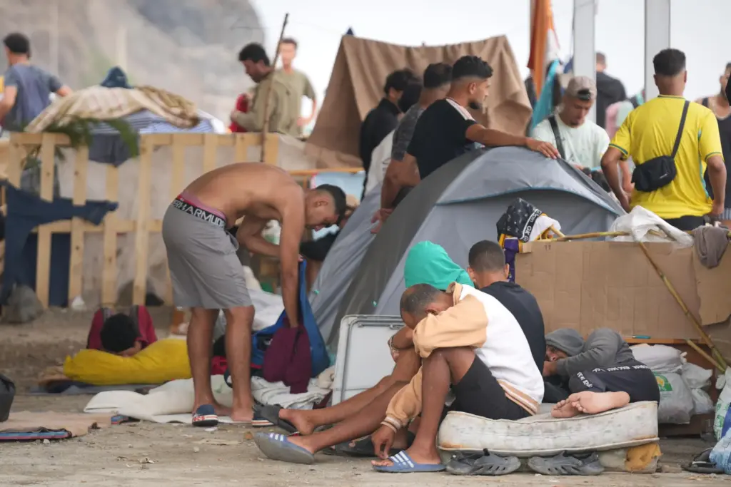 Migrants stand near their tents at El Trampolín beach in...