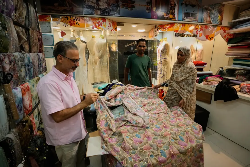 People examine embroidered fabric at a textile shop in a...