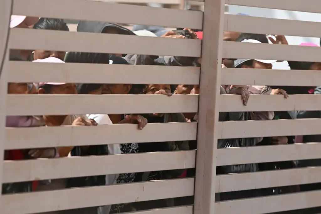 Relatives of crew members of the boat Maria Candelaria peer through a fence.