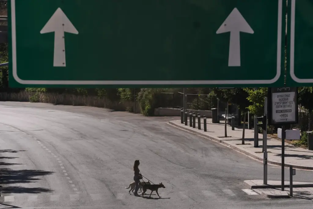 A woman walks with her dogs as they cross an empty street during Yom Kippur.