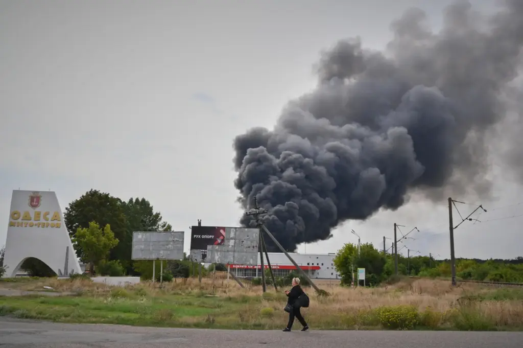 A woman walks by the burning warehouse at the city...