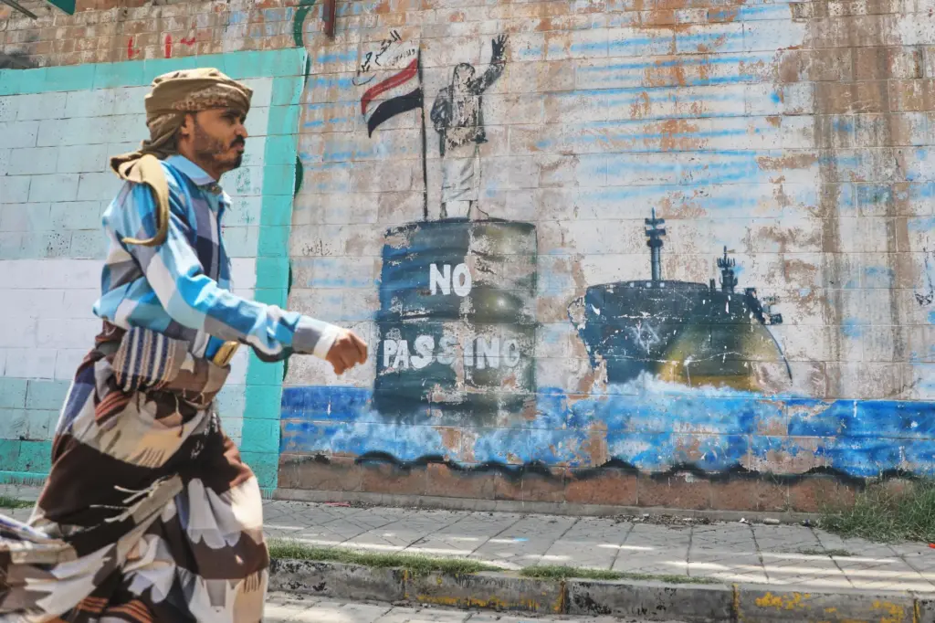 A man walks in front of a mural symbolizing shipping restrictions through the Bab el-Mandeb Strait.