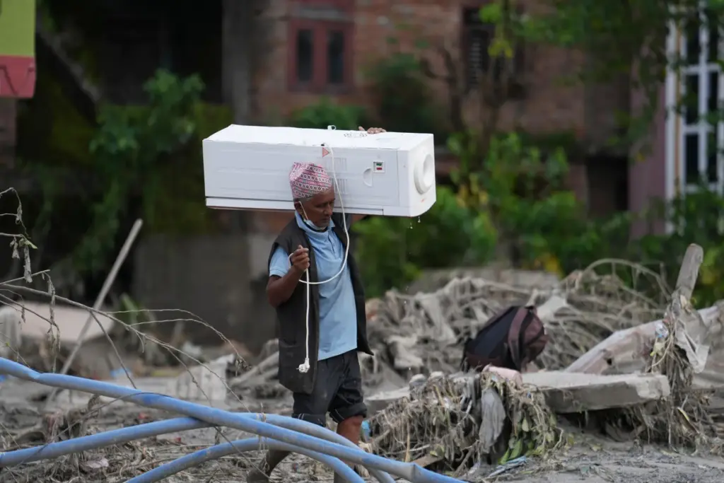 A resident carries an air cooler salvaged from his damaged house.