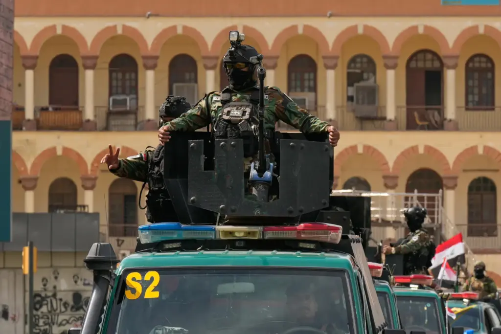 Iraqi security officers ride atop vehicles during a convoy.