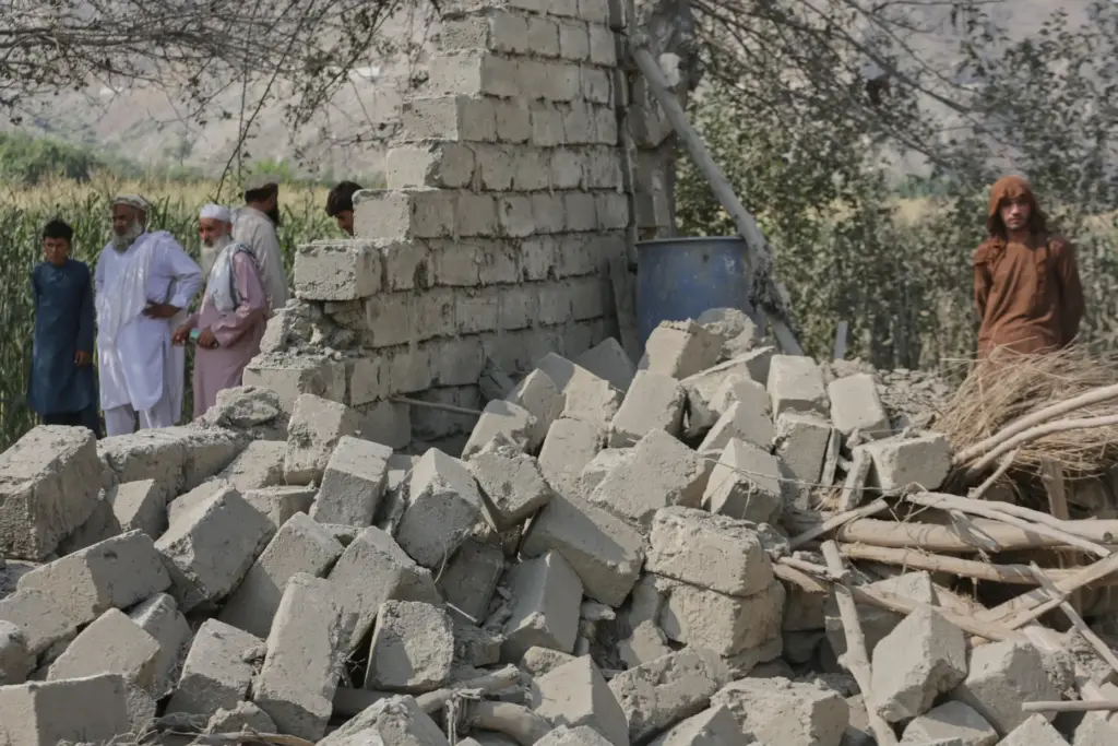 Residents stand near a collapsed wall of a house damaged...