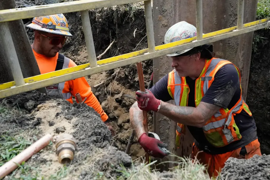 Workers install a copper pipe to replace a lead service...