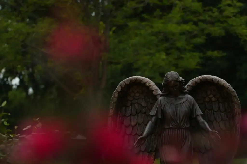 A sculpture of an angel stands the gardens at a memorial.