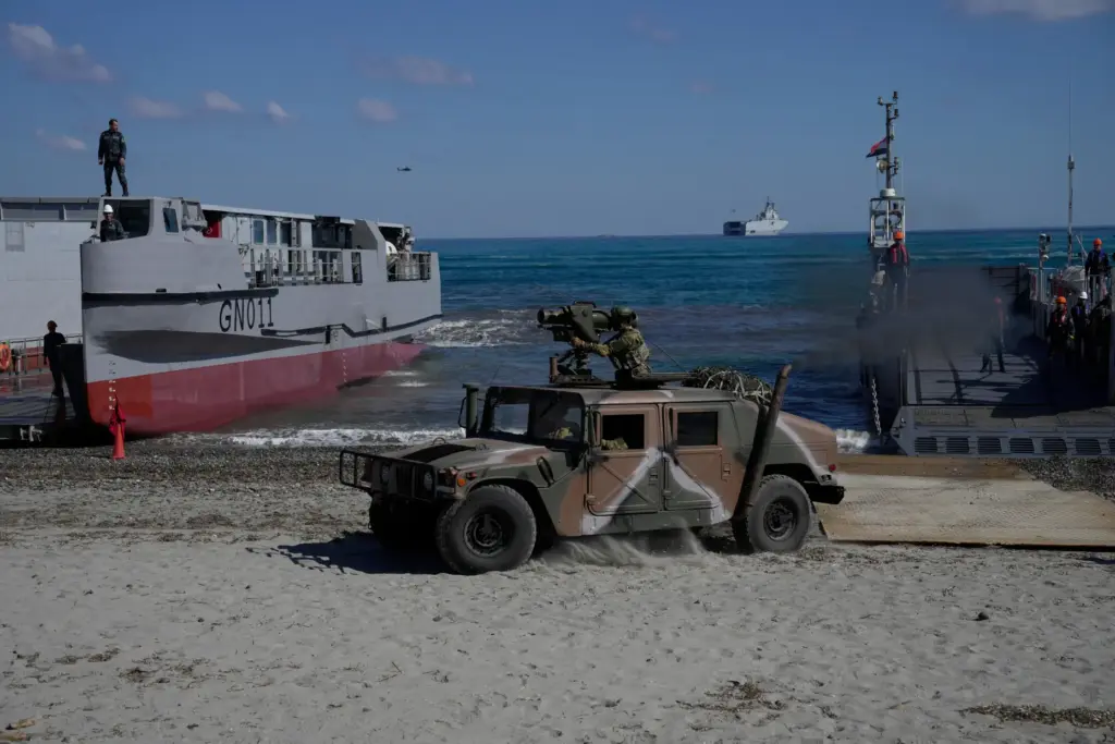 Greek service members drive a military vehicle ashore from a...