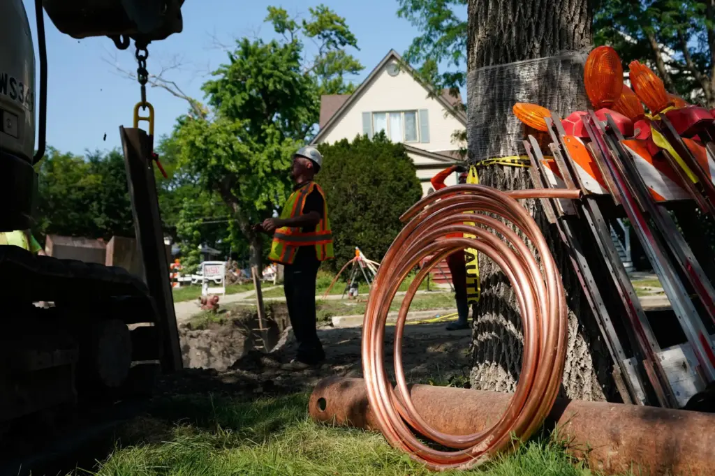 Copper pipe sits at right as a worker helps to...