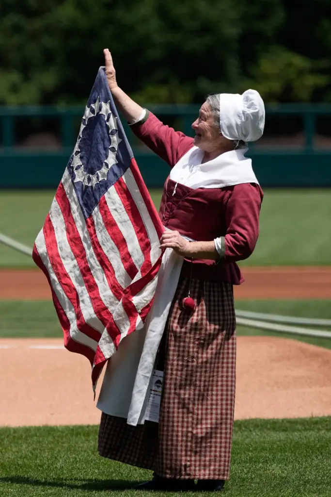 Carol Spacht as Betsy Ross, left, reacts before a baseball...