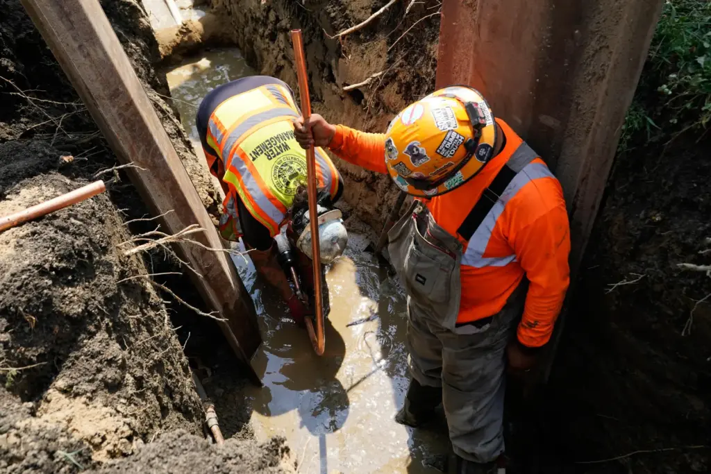 Workers install a copper pipe to replace a lead service...