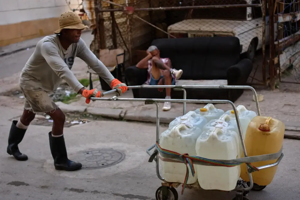 A man pushes a cart filled with water containers while...
