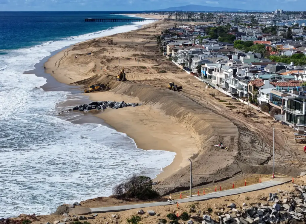 Workers build up a sand berm between homes and The...
