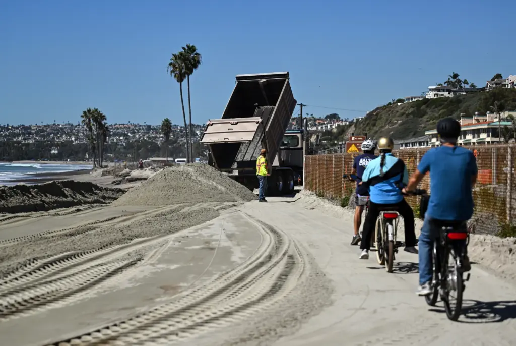 Beachgoers ride past new sand at Capistrano Beach in Dana...