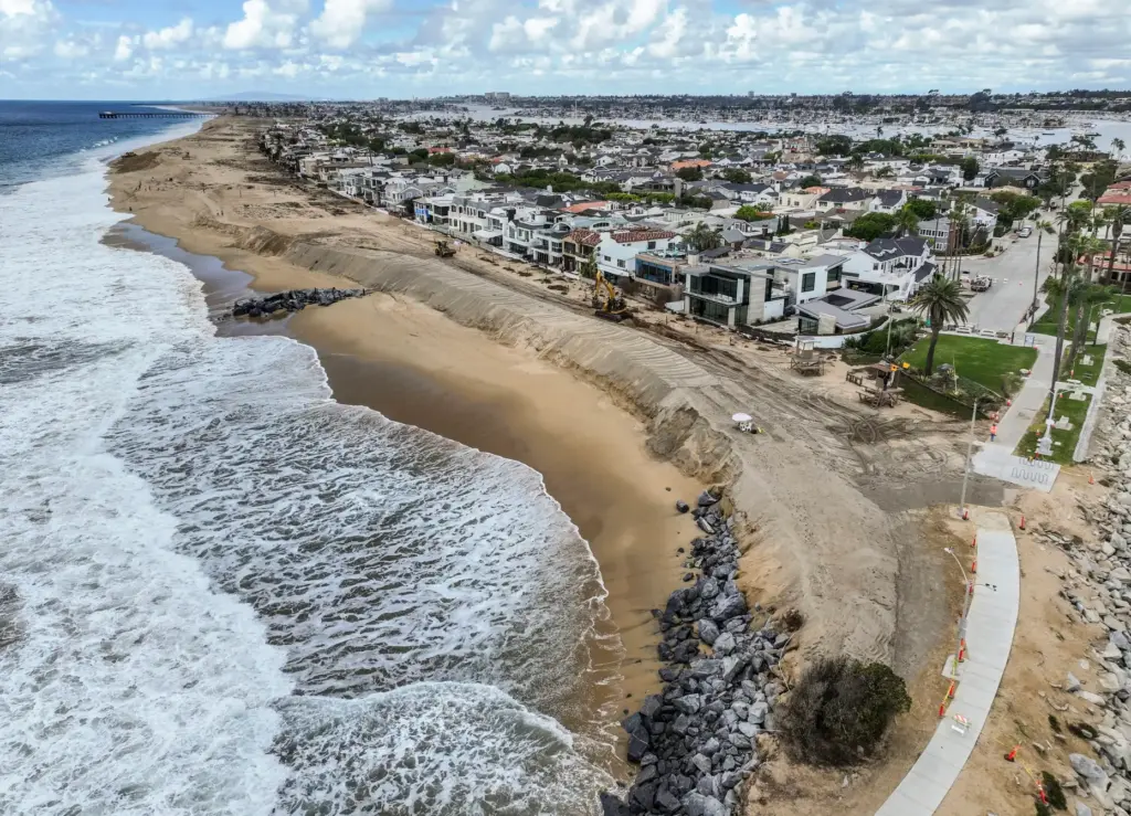 Workers build up a sand berm between homes and The...
