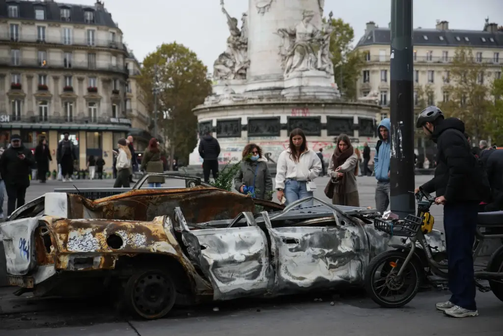 People watch a burned-out car after a quiet night Monday under curfew in Paris.