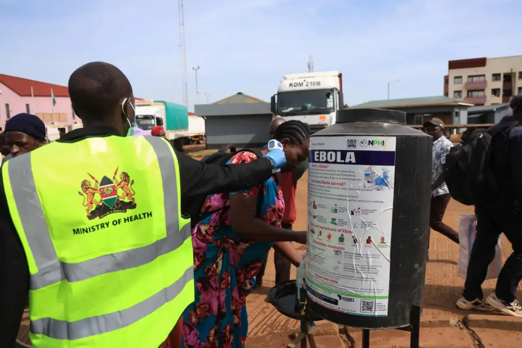 People disinfect their hands as a Kenyan health worker checks...