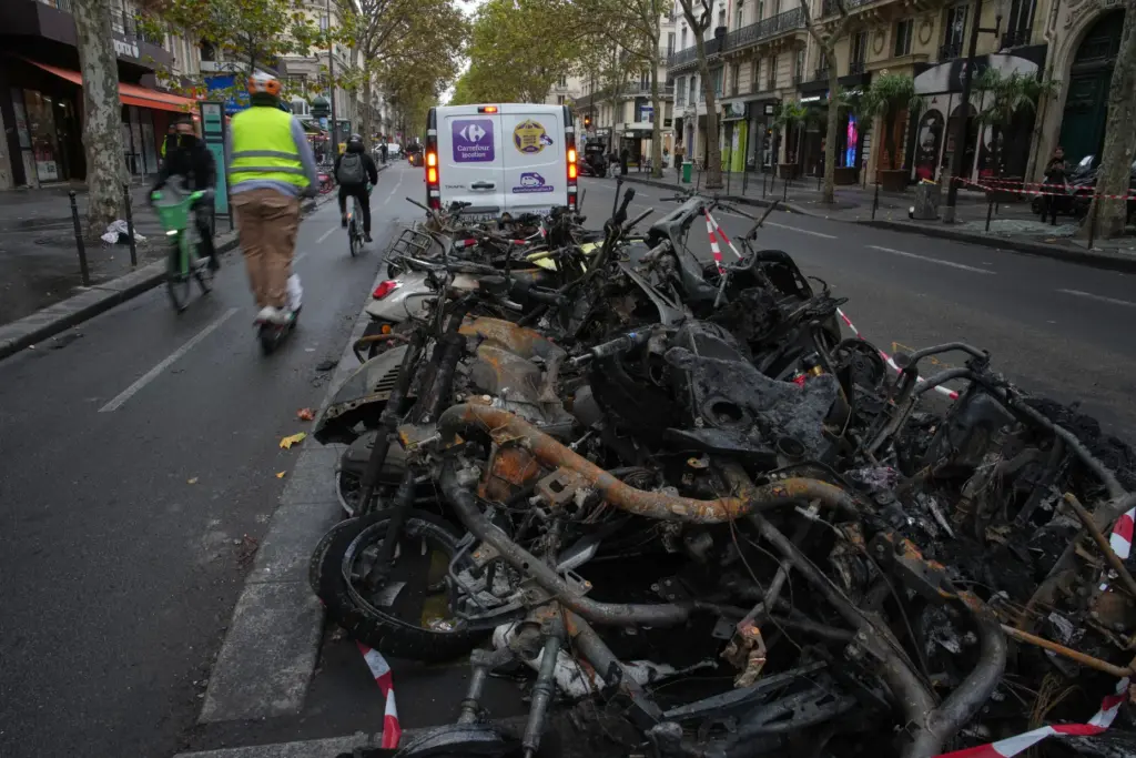 People ride past burned-out bikes after a quiet night Monday under curfew in Paris.