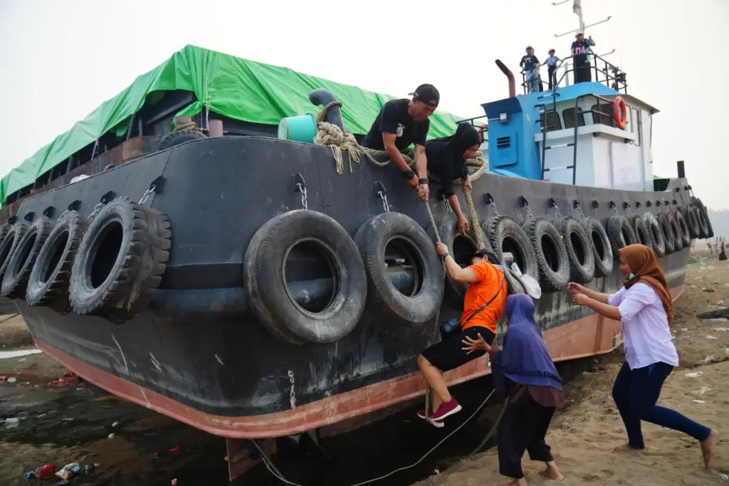 A man helps a woman climb aboard a tugboat grounded...