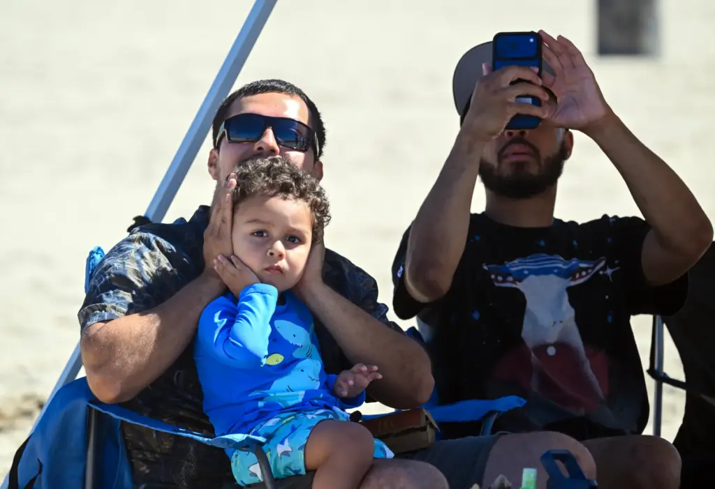 Luis Bernardino covers his sonâs, Leonardo Bernardino, ears as he...