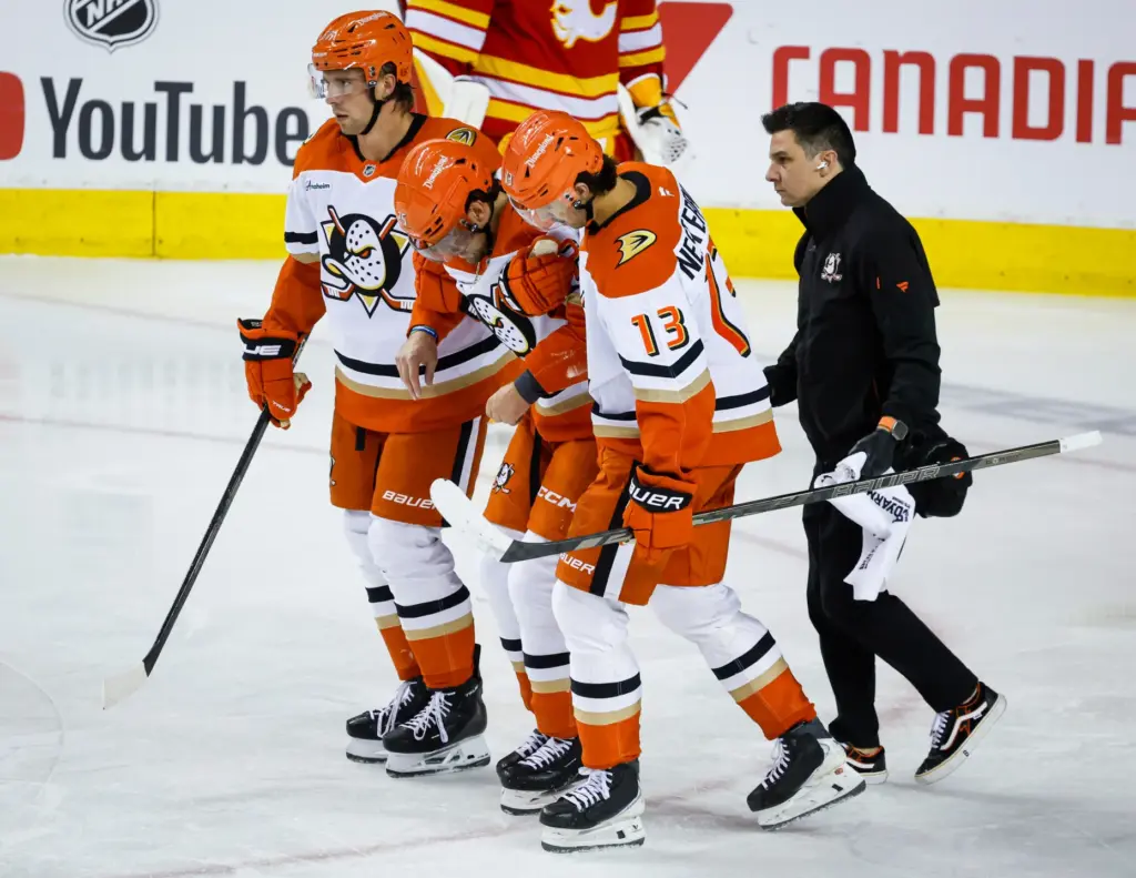 Ducks’ Ryan Poehling, center, is helped off the ice by...