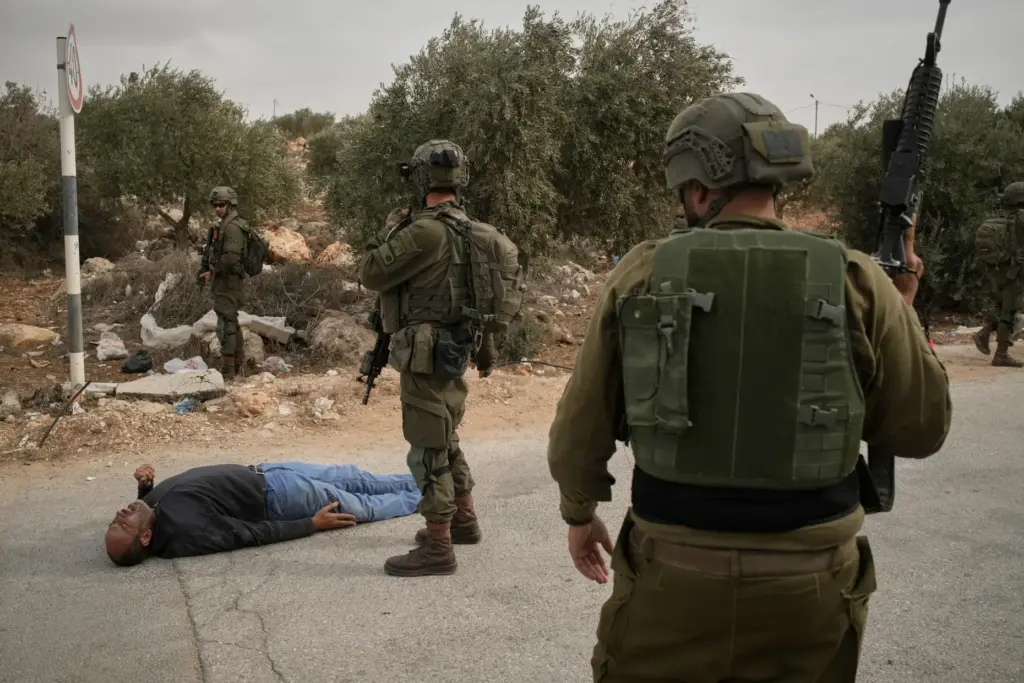 Israeli soldiers stand beside a wounded Palestinian man lying on...