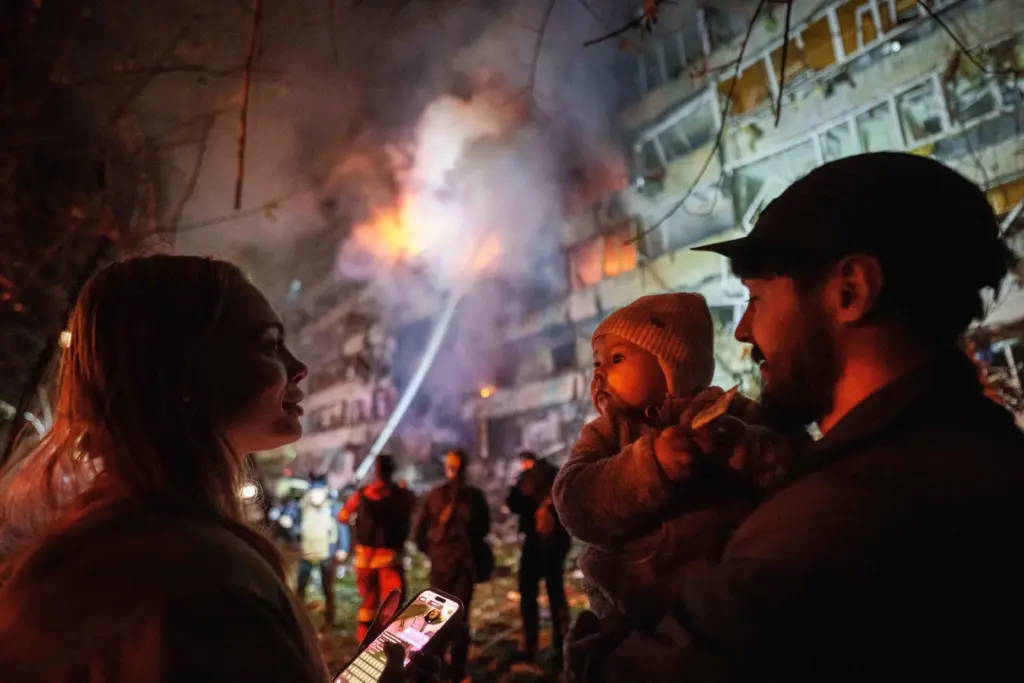 Victoria Deineko, her husband Ievhen Deineko and their daughter Mia look at a damaged building.