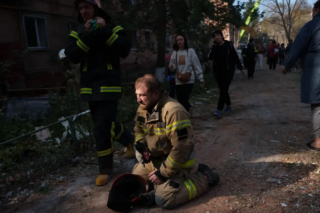 A rescue worker sits on the ground next to a building destroyed in a Russian strike.