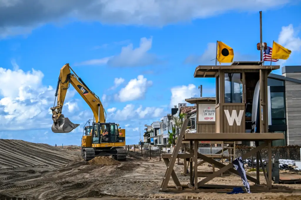 Workers build up a sand berm between homes and The...
