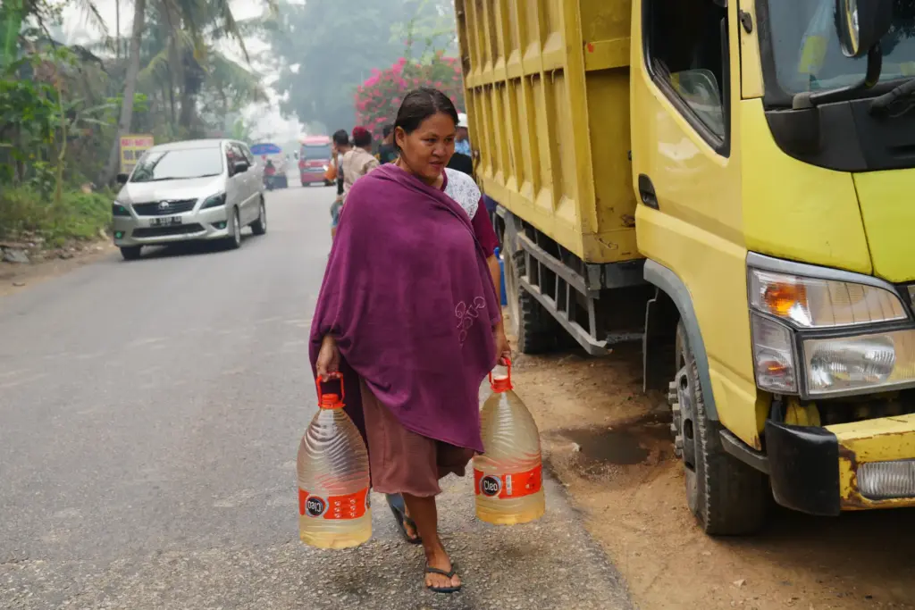 Sriwati, a shopkeeper and mother, carries two containers filled with...