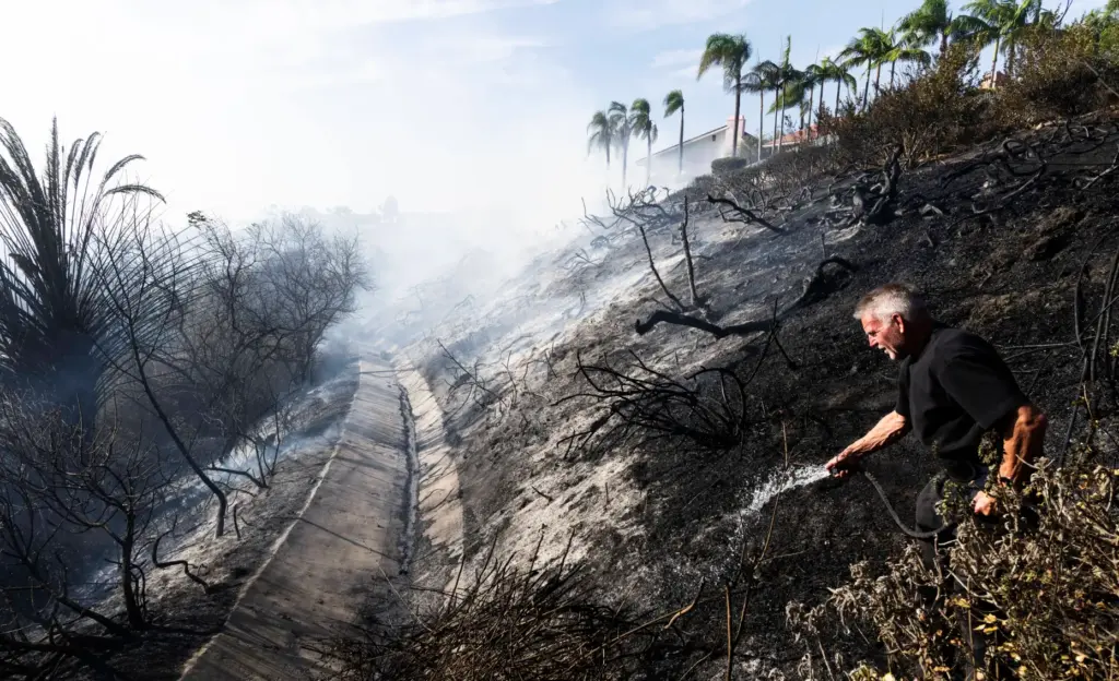 Homeowner Steve Taylor uses a garden hose to put out...