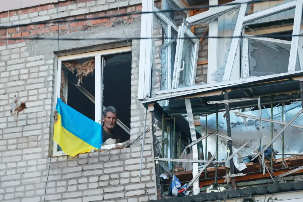 A man looks through a broken window in a residential house damaged by a Russian strike.