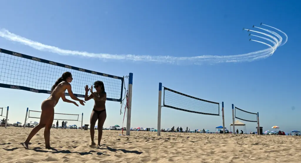 Beachgoers play volleyball as the Dawn Patrol Airshows Formation Team...