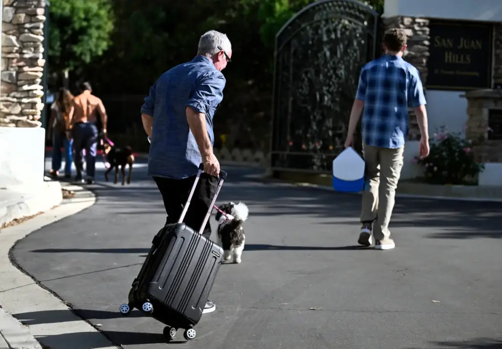 People return to their homes while pulling and carrying their...