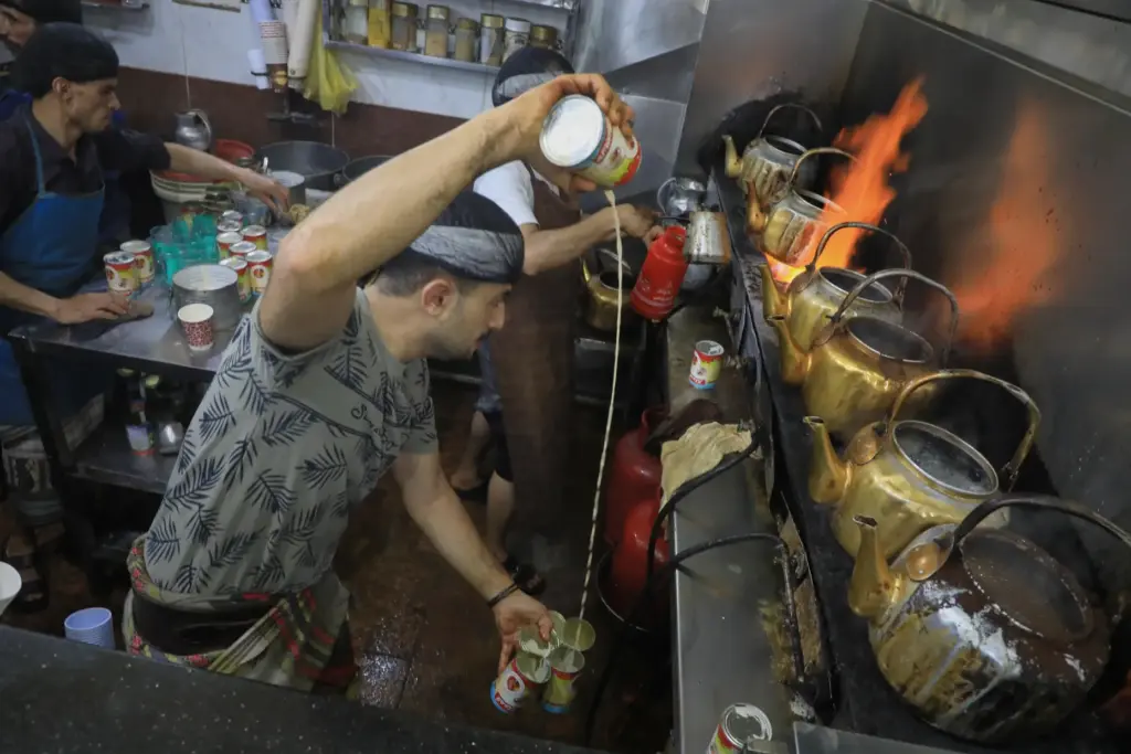 A tea seller pours milk from a can as he...