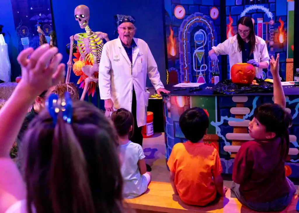 Volunteers raise their hands as Discovery Cube staff members Noah...