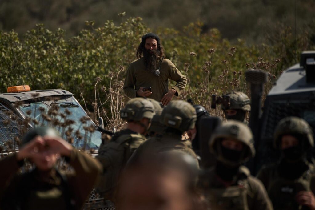 FILE – An Israeli settler overlooks members of Israeli forces...